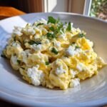 Close-up of fluffy scrambled egg topped with crumbled white cheese and fresh mint leaves.