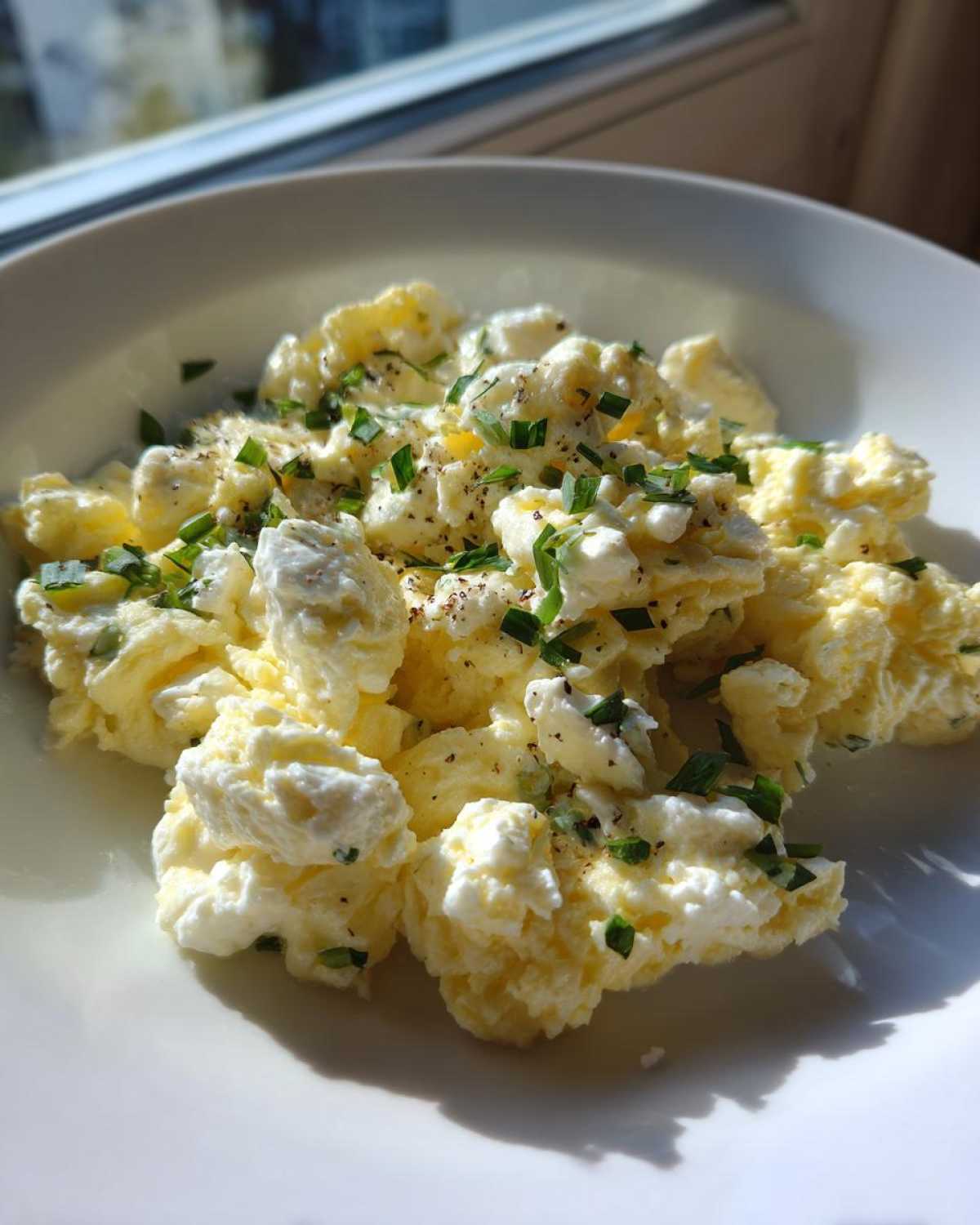 Close-up of fluffy, creamy scrambled egg curds topped with fresh chives and black pepper.
