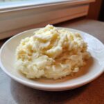 A close-up of creamy, fluffy garlic mashed potatoes topped with melting butter served in a white bowl.