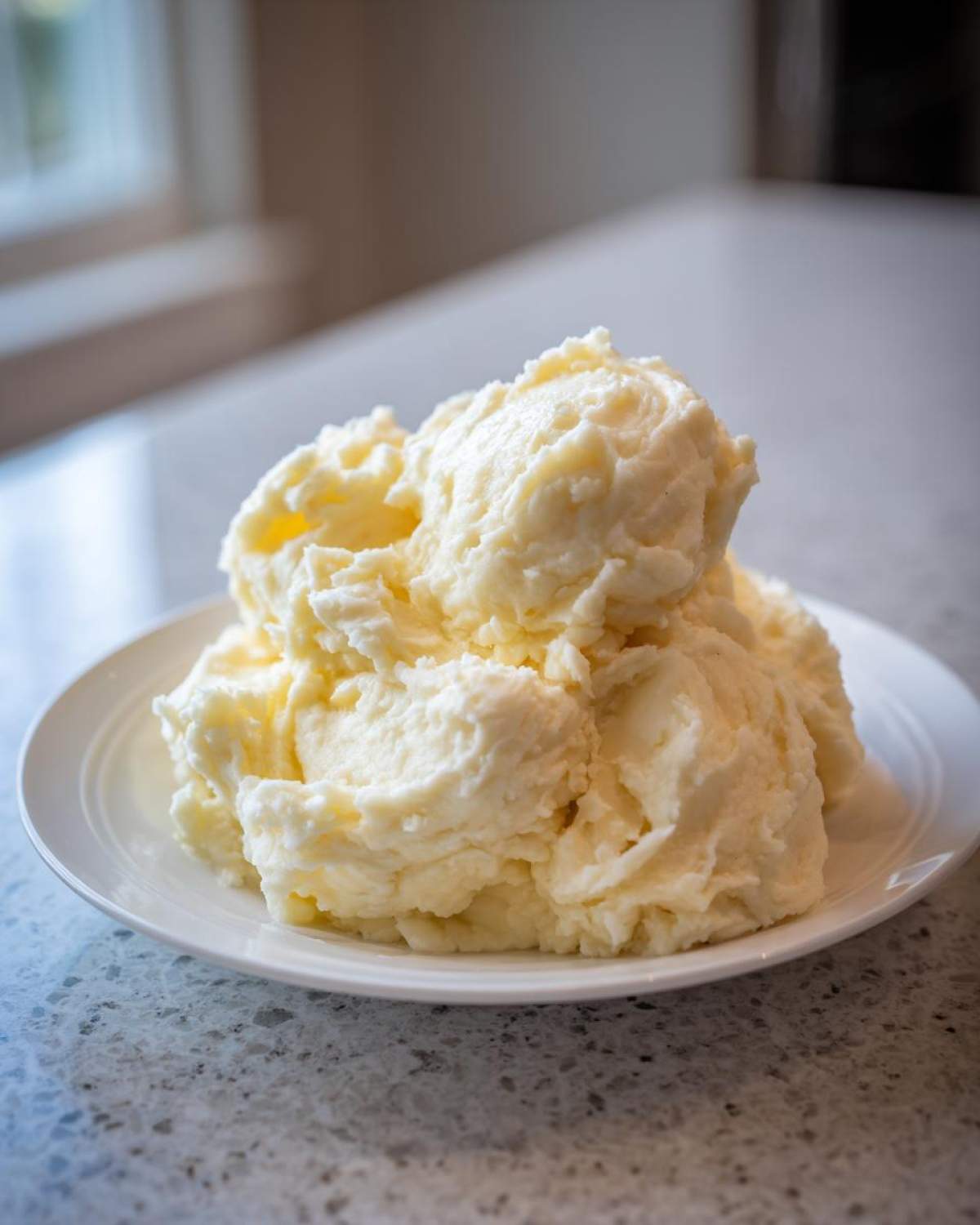 A generous serving of creamy, fluffy garlic mashed potatoes piled high on a white plate.