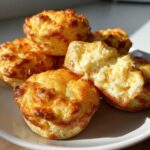 A stack of golden brown, fluffy baked egg bites, with one cut open showing the airy interior.