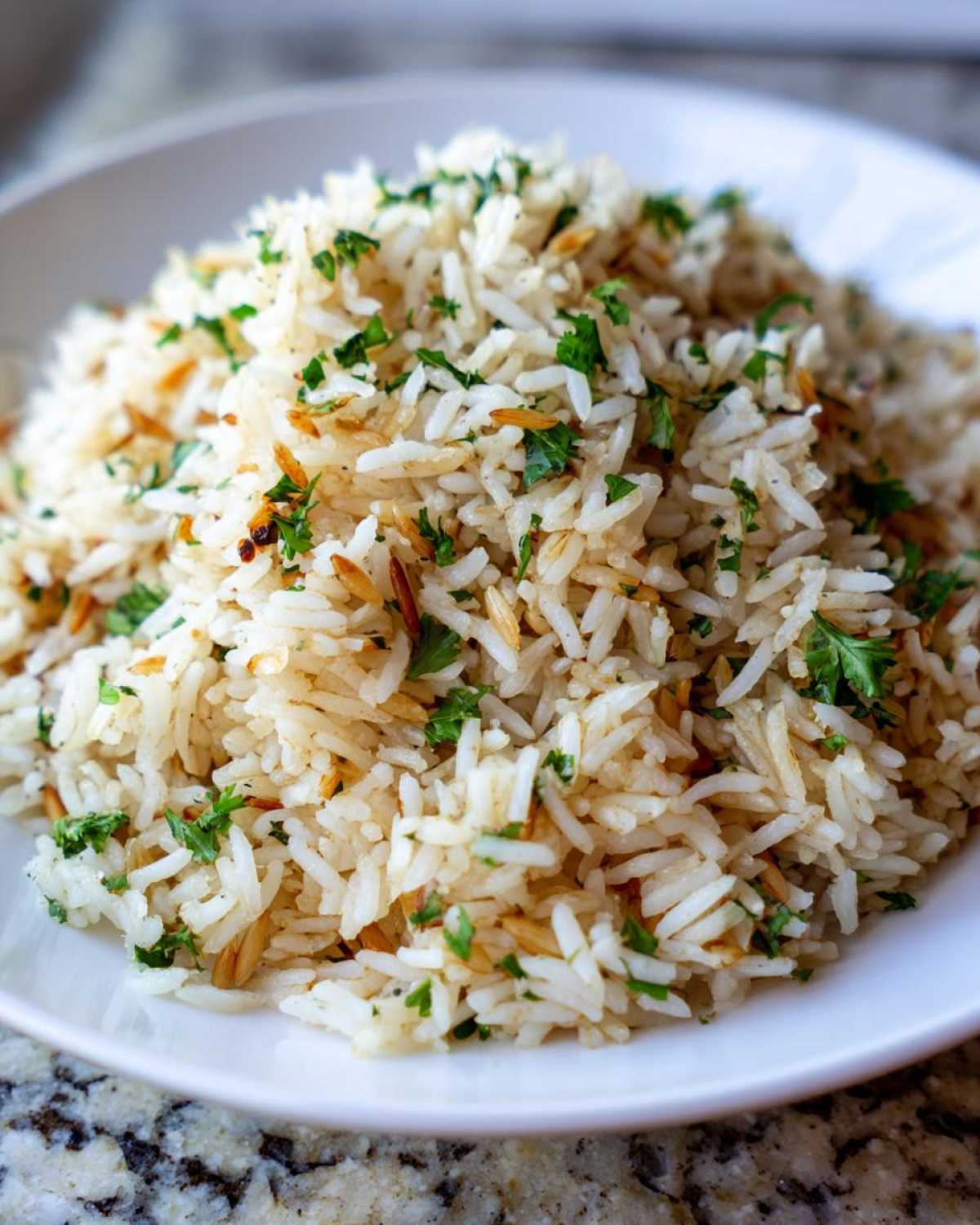 Close-up of fluffy rice pilaf mixed with toasted vermicelli and fresh chopped parsley served in a white bowl.