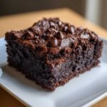Close-up of a fudgy square of black bean brownies topped with melted chocolate chips on a white plate.