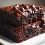 Close-up of two fudgy black bean brownies stacked, topped with melted chocolate chips.