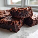 Close-up of three fudgy sweet potato brownies stacked, showing a rich, dark interior and chocolate chips.