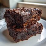 Two stacked, fudgy sweet potato brownies topped with melted chocolate chips on a white plate.