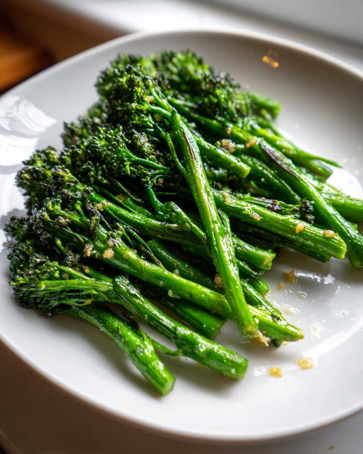 Close-up of bright green, tender broccolini stalks seasoned with garlic and lemon juice on a white plate.