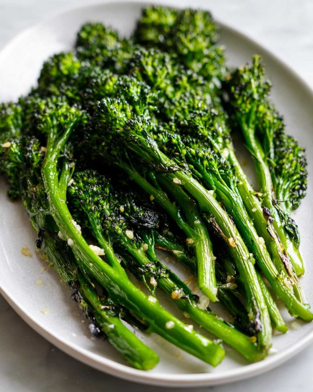 Close-up of bright green, cooked broccolini seasoned with garlic and lemon, served on a light gray plate.