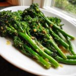 Close-up of bright green, roasted broccolini tossed with garlic and lemon juice on a white plate.