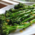 Close-up of bright green, sautéed broccolini tossed in garlic and lemon sauce on a white plate.