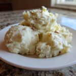 Three scoops of fluffy garlic mashed potatoes, flecked with browned bits, served on a white plate.