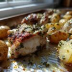 Close-up of golden brown garlic parmesan chicken and potatoes fresh from the oven on a baking sheet.