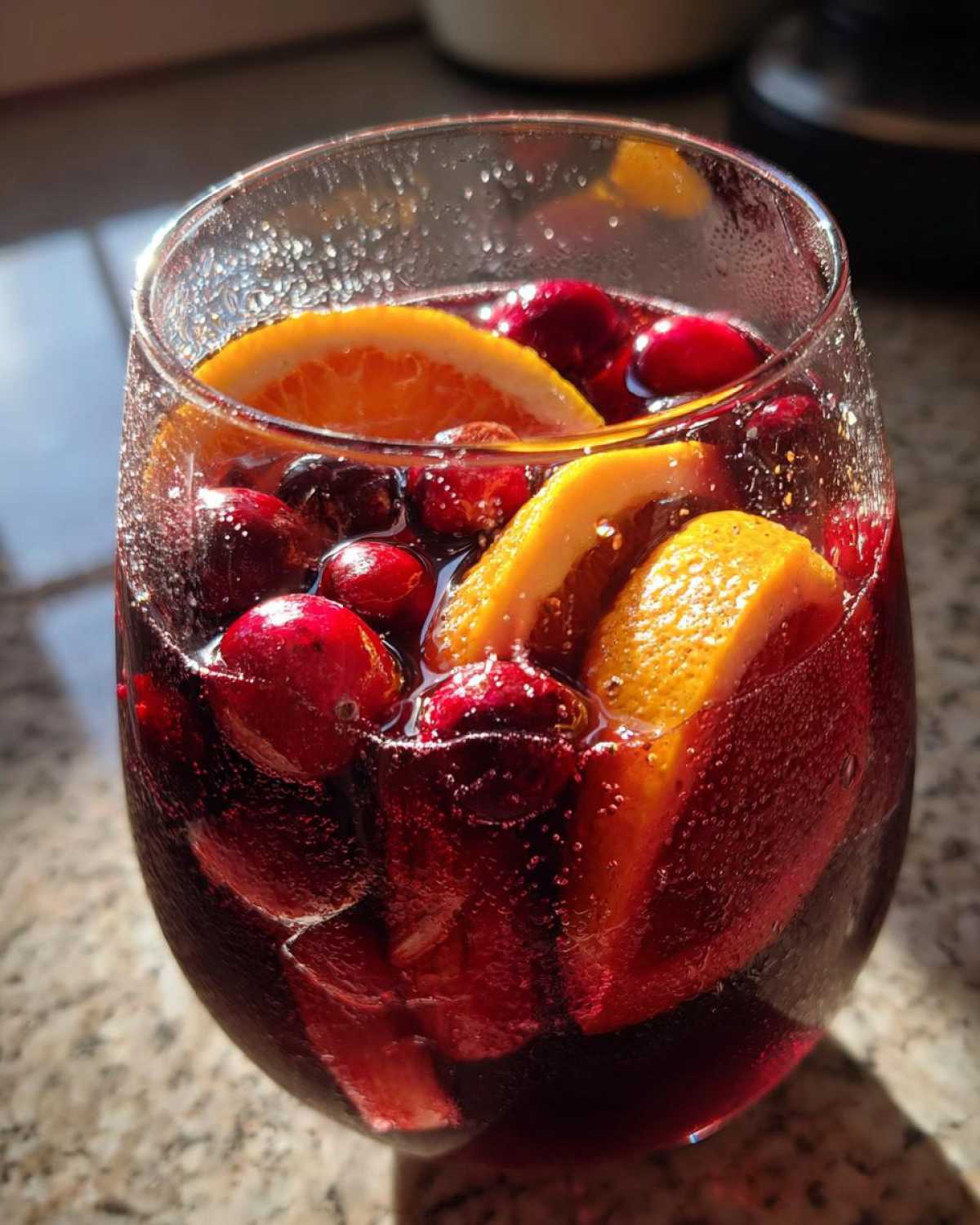 Close-up of a glass filled with bubbling Christmas sangria, featuring slices of orange and whole cranberries.