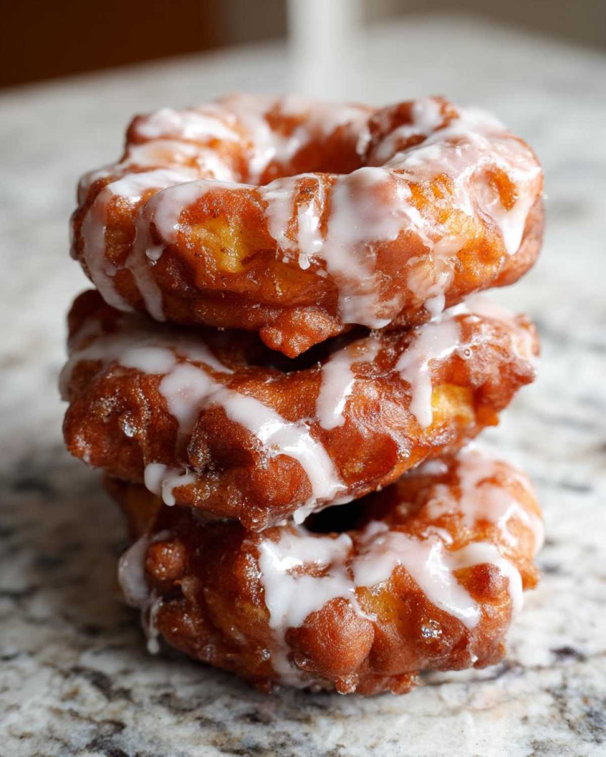 A stack of three golden brown, deep-fried apple fritter donuts drizzled with white icing.
