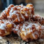 Close-up of a stack of golden brown, freshly fried apple fritter pieces drizzled heavily with white vanilla glaze.