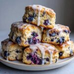 A stack of freshly baked blueberry scones drizzled generously with white lemon glaze.