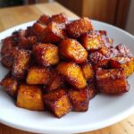 A close-up shot of perfectly caramelized and glazed roasted sweet potato cubes piled high on a white plate.