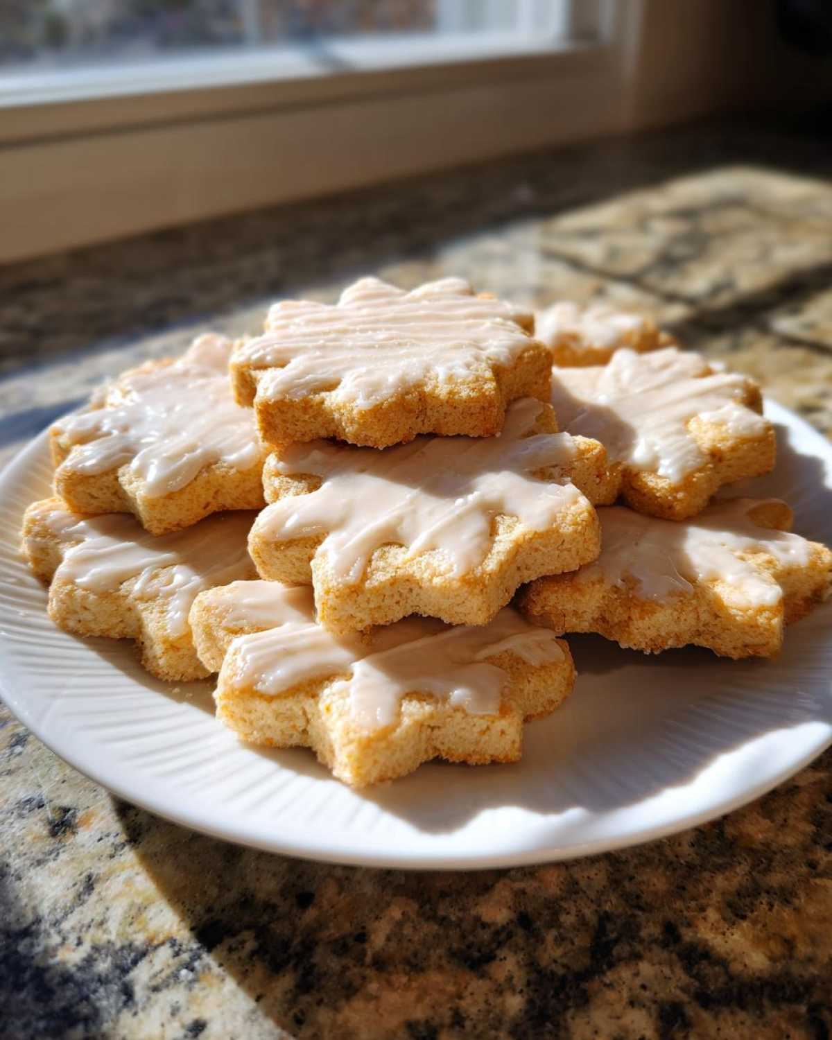 A stack of star-shaped vegan sugar cookies topped with a thin white glaze, resting on a white plate.