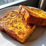 Close-up of two golden brown, thick-cut slices of perfectly cooked french toast on a white plate.