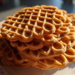 A close-up stack of golden brown, crisp pizzelle cookies with their signature waffle pattern.