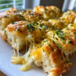 Close-up of gooey, melted cheese pulling apart from a section of baked cheese bread topped with parsley.