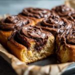 Close-up of gooey chocolate cinnamon rolls, one roll is broken open showing the soft interior.