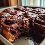 Close-up of gooey chocolate cinnamon rolls in a baking pan, one roll has a bite taken out showing the soft interior.
