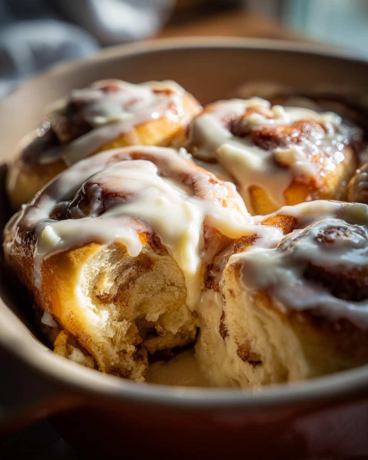 Close-up of freshly baked cinnamon roll with thick white icing, one roll pulled apart showing soft interior.