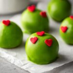 Close-up of bright green Grinch Oreo balls decorated with small red candy hearts, resting on parchment paper.
