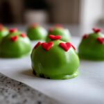 A close-up, shallow depth of field shot of bright green Grinch Oreo Balls decorated with small red heart sprinkles.