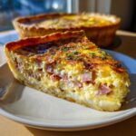 A close-up slice of Ham and Cheese Quiche showing chunks of ham in the creamy egg filling, garnished with parsley.