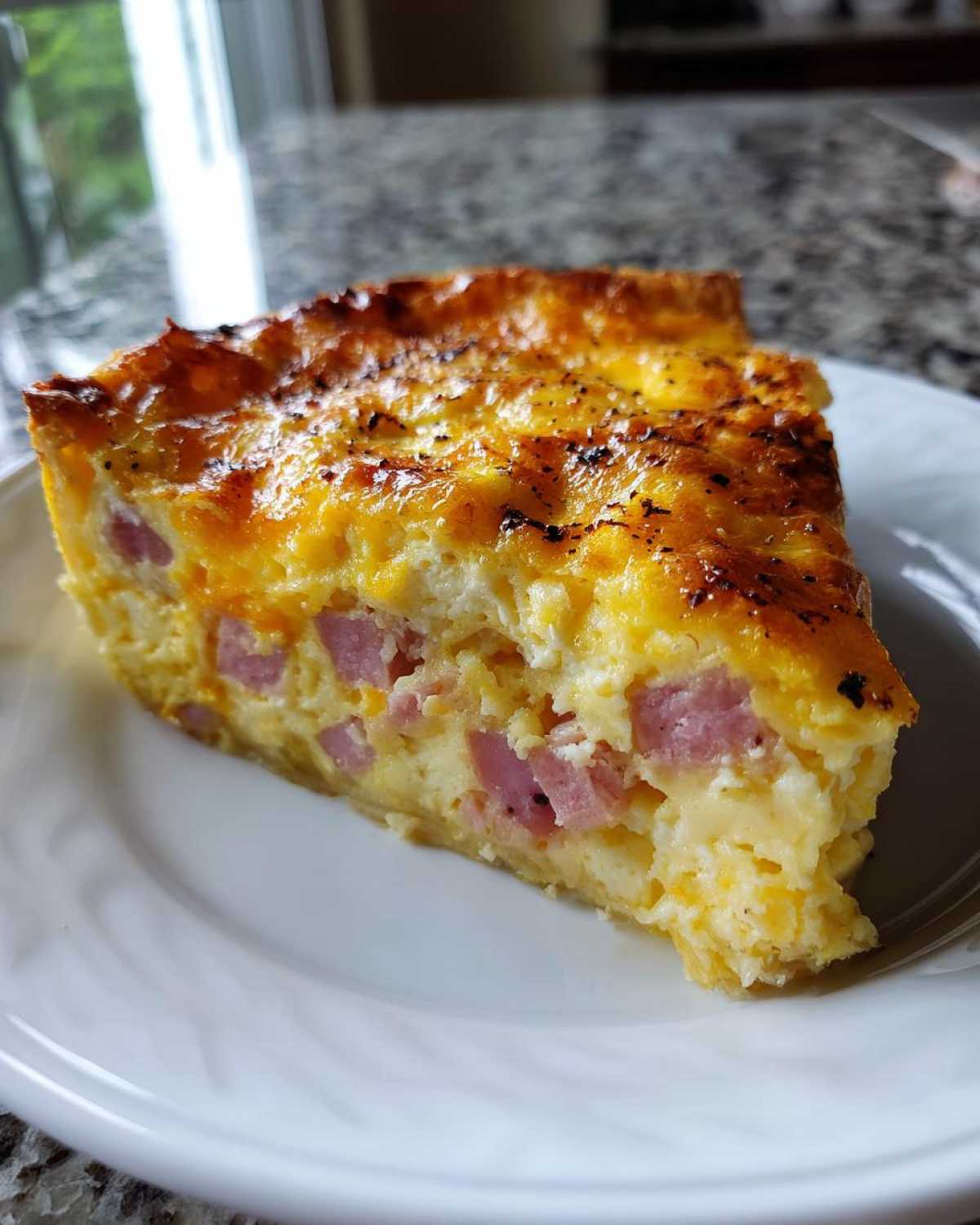 Close-up of a thick slice of Ham and cheese quiche with visible chunks of ham in a fluffy egg and cheese filling.