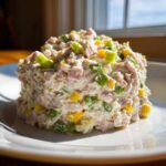 A mound of creamy ham salad recipe mixed with diced green and yellow peppers served on a white plate.