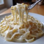 A fork lifts fettuccine coated in creamy homemade alfredo sauce, showing a cheese pull.