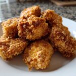 A pile of crispy, golden brown homemade chicken nuggets served on a clean white plate.
