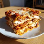 A thick, layered slice of homemade lasagna with rich meat sauce and melted white cheese on a white plate.
