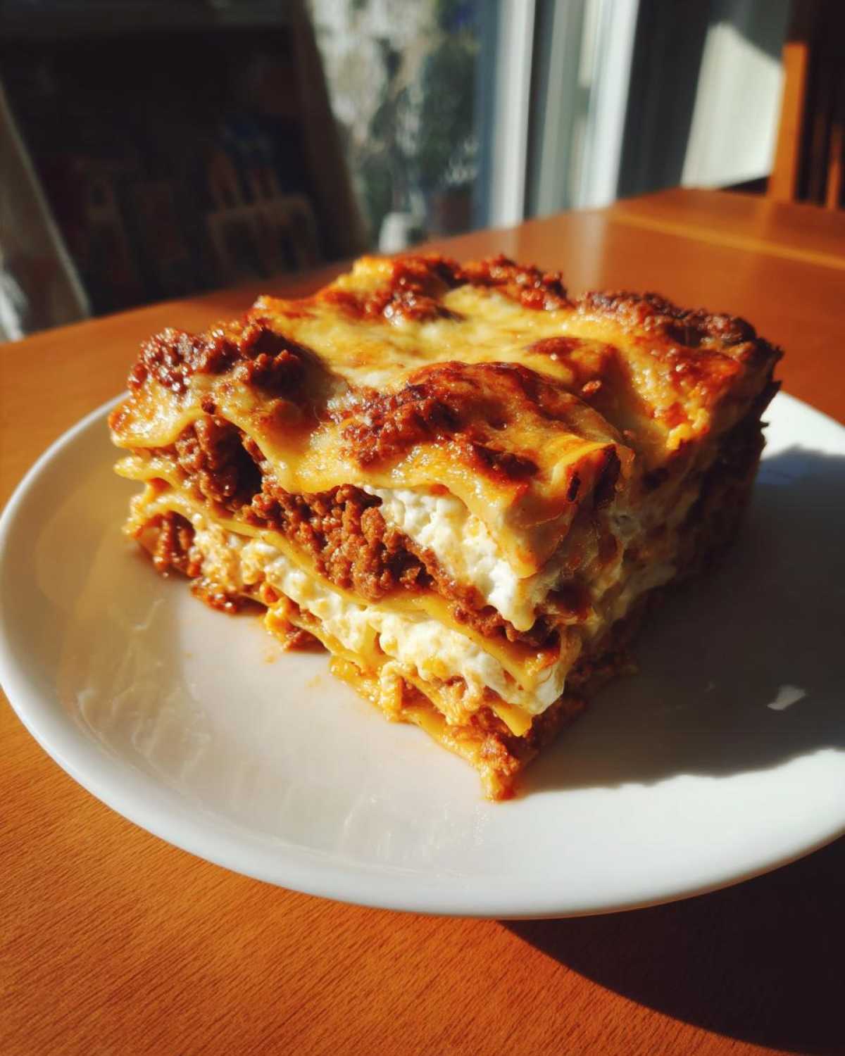 A close-up, sunlit slice of homemade lasagna showing layers of pasta, meat sauce, and ricotta cheese.