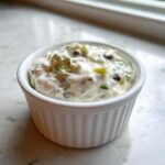 Close-up of a creamy, chunky homemade tartar sauce recipe served in a small white fluted ramekin.