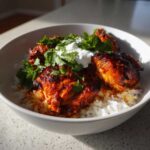 Close-up of glazed, spicy harissa chicken pieces served over white rice, topped with yogurt and fresh cilantro.