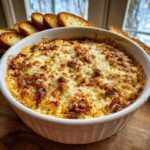 A close-up of a hot, baked reuben dip topped with melted, browned cheese, served with toasted bread slices.