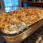 A close-up of a freshly baked hot chicken salad casserole with a golden, crunchy topping in a clear glass baking dish.