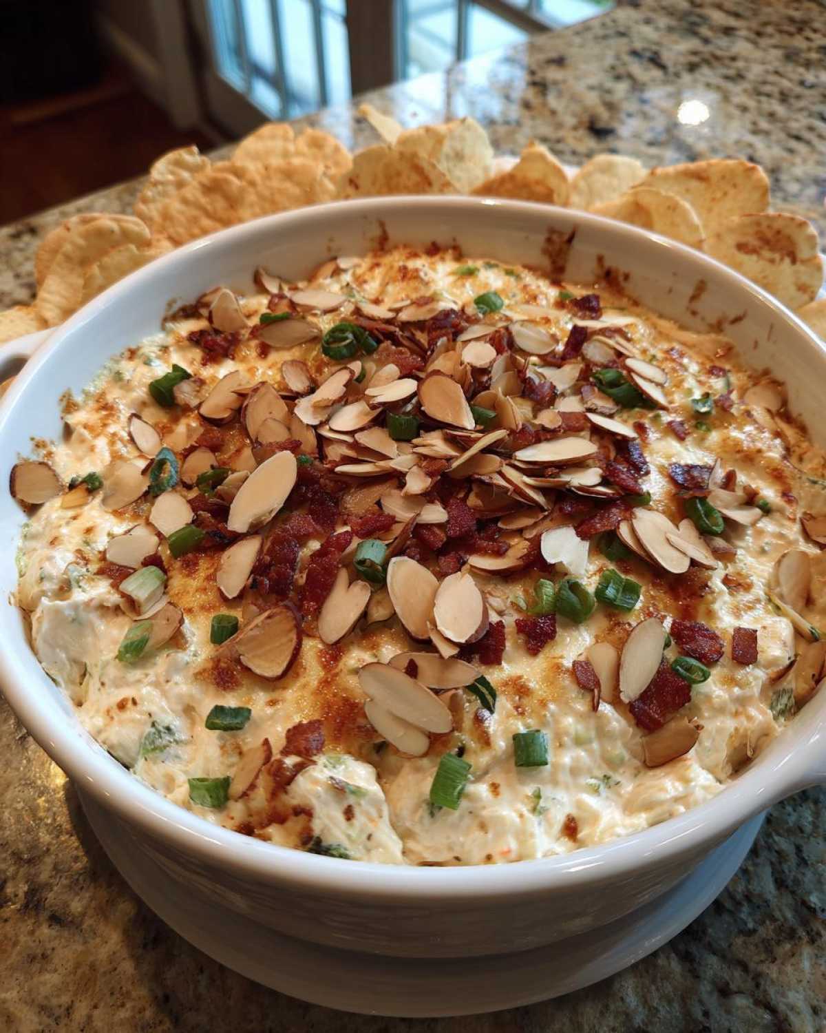 A baked Neiman Marcus dip served hot in a white dish, topped generously with sliced almonds, bacon bits, and green onions.