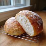 A loaf of amazing italian bread, cut in half showing the airy white crumb and golden crust dusted with flour.