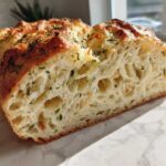 Close-up of the airy interior crumb of an Italian herb and cheese bread loaf, showing melted cheese pockets and green herbs.