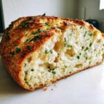 Close-up of a freshly baked Italian herb and cheese bread loaf, showing the soft, airy interior studded with green herbs.