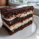 A rich, multi-layered slice of chocolate Italian love cake featuring alternating dark cake and white cream layers, topped with ganache.