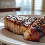 Close-up of a perfectly cooked, juicy pork steak recipe with a dark, glistening glaze on a white plate.