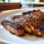 Close-up of a perfectly cooked, juicy pork steak recipe slice covered in a savory, grainy glaze.