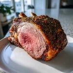 A cross-section of a juicy, medium-rare rib roast showing a thick herb crust and exposed bones.