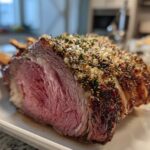 Close-up of a perfectly cooked, medium-rare rib roast showing a thick herb and garlic crust.